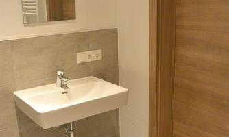 A modern bathroom with a sink and a mirror. The walls are in neutral colors and the door is made of wood.