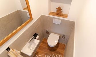 A modern bathroom with a toilet and a sink. On the wall is a large mirror and a decorative element on a shelf.