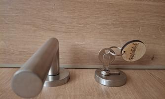 A stainless steel door handle on a wooden door with a set of keys. The key has a tag that says "Summit View."