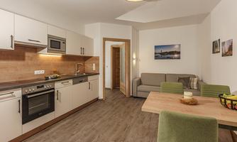 Modern kitchen with bright furniture and an inviting dining area. The room is well-lit and comfortably furnished.
