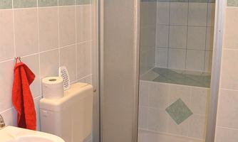 A small bathroom with a shower, a toilet, and a sink. The walls are tiled in light colors, and a red towel hangs on the wall.