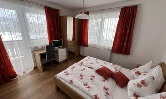 A cozy bedroom with a double bed and beautiful rose bedding. Large windows with red curtains let in a lot of light.