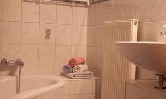 A bathroom with a bathtub and a sink. Colorful towels are neatly stacked.