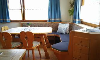 A cozy dining area with a large table and a bench-like seating option. The windows let in plenty of light and the blue curtains create a friendly atmosphere.