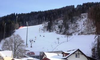 A snowy mountain landscape with a ski lift and slopes in the background. In the foreground, there are some cozy houses visible.