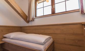 A cozy room with wood paneling and a single bed. A large window provides plenty of natural light.