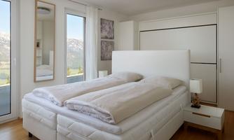 A modern bedroom with a large double bed and bright windows. The elegant decor creates a calm and inviting atmosphere.
