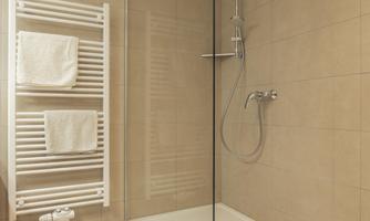A modern bathroom with a glass shower and light tiles. Fresh towels hang on a towel warmer in the background.