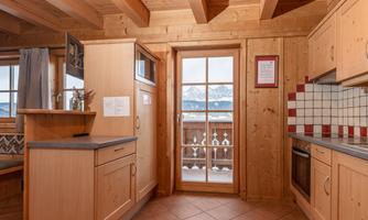 A modern wooden kitchen with windows and a view of the mountains. The space is bright and welcoming.