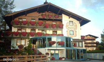 A traditional, beautiful building with blooming balcony flowers. The architecture is rustic and inviting, surrounded by green countryside.