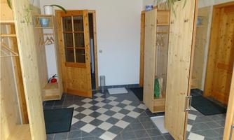 A bright entrance area with wood paneling and large mirrors. The floor is laid out in a checkerboard pattern and plants hang over the coat racks.