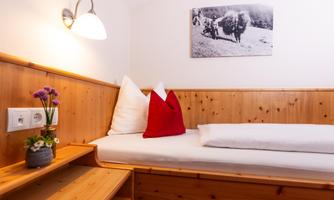 A cozy sleeping area with wood paneling and a single bed. A small bouquet of flowers is on the nightstand and a black-and-white picture hangs on the wall.