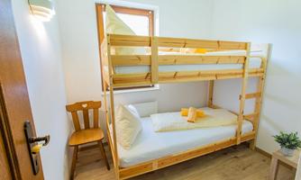 A simple room with a wooden bunk bed and a single bed. The room is bright and furnished with minimalist furniture.