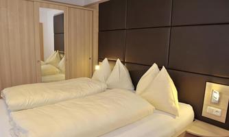 A modern bedroom with two beds and pillows in a bright setting. A mirror and elegant wooden paneling give the room a cozy atmosphere.