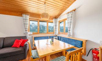 A bright room with a large table and chairs. Through the windows, there is a beautiful view of the mountains.