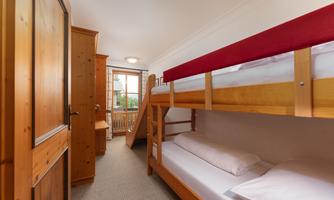 A cozy bedroom with a wooden bunk bed and a desk. The room has a window with a view outside and warm, inviting colors.