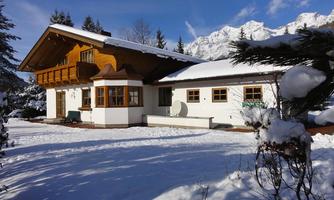 A beautiful house in the snow with a traditional wooden design. In the background, snow-covered mountains and a clear sky can be seen.