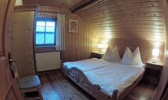 A cozy bedroom with wooden-paneled walls. The room has a double bed, nightstands, and a window facing outside.