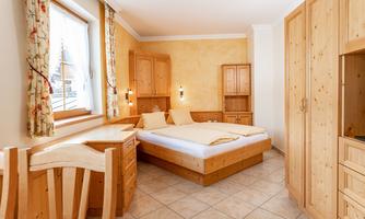 A cozy bedroom with wooden furniture and a double bed. The walls are painted in warm yellow tones, and there is a window with curtains.