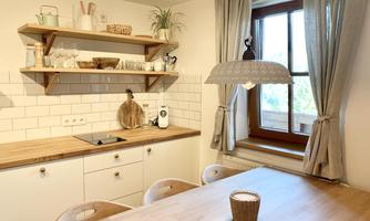 A bright kitchen with wooden shelves and a large dining table. The windows let in plenty of light and create an inviting atmosphere.