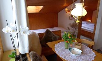 A cozy dining area with a paneled wooden wall and a friendly atmosphere. Fresh flowers and a lovely tablecloth adorn the table.