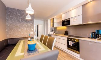 Modern kitchen with elegant furnishings and a dining area. A table with a blue bowl and wine bottle is the centerpiece.