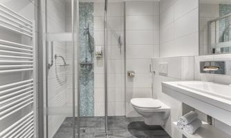 A modern bathroom with a shower and toilet. The walls are light tiled, and there is a towel warmer as well as a sink area.