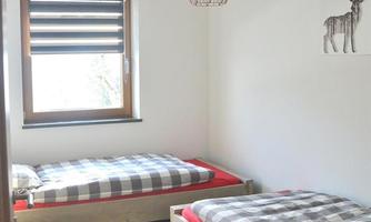 A simple bedroom with two beds and a wooden crib. The room has a window with blinds and a modern lamp.