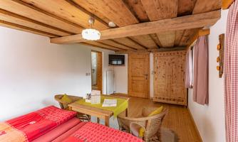 A cozy room with wooden ceilings and a rustic furniture style. There are two beds, a table, and a wooden wardrobe.