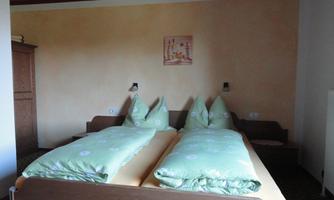 A simple room with two single beds and green bedspreads. The wall is painted in warm colors, and there is a picture above the bed.