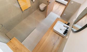 A modern bathroom with a shower, a sink, and a wooden surface. The walls are in neutral tones, and a towel hangs on the wall.