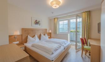 A modern hotel room with a double bed and two bedside tables. The room has large windows that offer a view of the mountains.