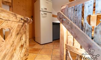 A cozy kitchen corner with a refrigerator and rustic wooden elements. The floor is tiled, and the atmosphere is warm and inviting.