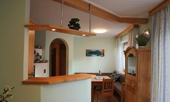 A cozy living kitchen with wooden details and a dining area. The room has light walls and a window with a view outside.