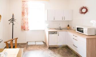 A bright and modern kitchen with white furniture and a large window. The room is well-lit and invites cooking.