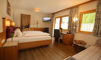 A cozy hotel room with a double bed and wooden furniture. Large windows provide plenty of daylight and a pleasant atmosphere.