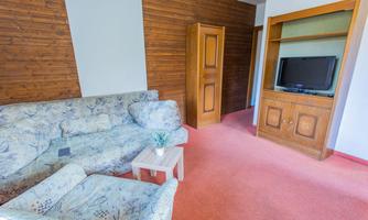 A cozy living room with a sofa and a small table. A television is hanging on the wall, and there is a wooden cabinet in the background.