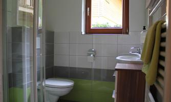 A modern bathroom with a shower, a toilet, and a sink. The walls are designed in gray and green tones, and a window provides natural light.