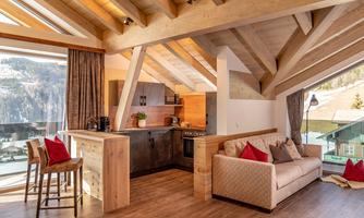 A modern apartment with wooden beams and large windows. The open kitchen and the cozy living area offer a beautiful view of the landscape.