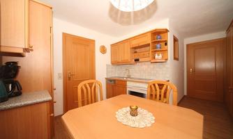 A cozy kitchen with wooden cabinets and a round dining table. There is also a stove and a dishwasher as well as a coffee machine on the countertop.