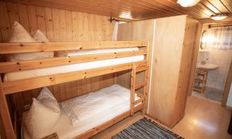 A simple bedroom with a wooden bunk bed. The room has wooden paneling and a small wash area.