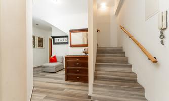 A bright entrance area with a staircase and a cozy seating area. The walls are painted light and there are decorative elements like a mirror and artworks.