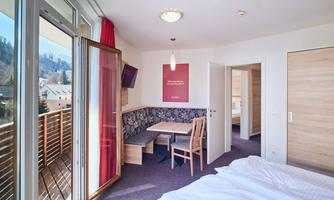 A bright guest room with a balcony and mountain view. There is a dining table and modern furniture.