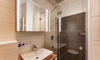 A modern bathroom with a shower and a sink. The walls are bright, and there are stylish mirrors and lighting.