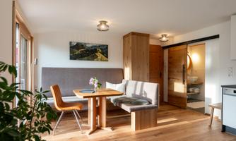 A modern apartment with a bright living area and a dining table. The decor is stylish with wood and a large window that lets in plenty of light.