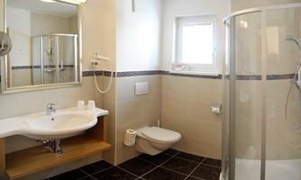 A modern bathroom with a shower, sink, and a large mirror. The walls are brightly tiled and the floor is dark.