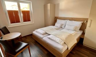 A cozy bedroom with a double bed and wooden floor. There is a small table and chairs as well as a window with blinds.