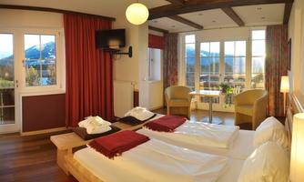 A cozy hotel room with two single beds and a beautiful view of the mountains. There is a dining table as well as bright daylight through large windows.