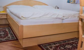 A cozy bedroom with a double bed and a light wood look. The floor is covered with a carpet, and there is a table nearby.