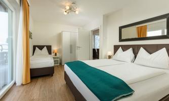 A modern room with two beds and bright colors. Large windows let in a lot of light, and there is a nice view outside.